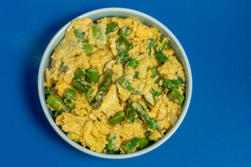 A traditional Alentejo dish, featuring scrambled eggs mixed with vibrant green asparagus. The golden hues of the eggs contrast beautifully with the deep blue background.