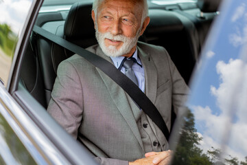 Senior gentleman in a sharp suit smiling while buckled up in his car