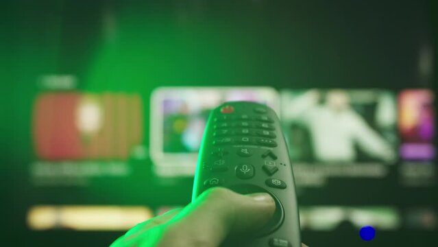 Woman with remote in hand switching channels, smart tv technology internet video content, screen with movie content at the background close up shot.