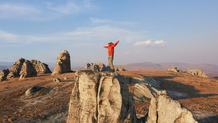 Active man tourist climbs to top of rock tower monolith as rock climber in nature. At top hiker raises his hands to sides from joy of success freeway flight, enjoying view of mountains at sunset light