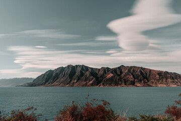 clouds with curious shapes over a range of impressive rocky mountains on the shores of the great blue lake in a quiet and lonely place in the middle of nature, hawea lake, new zealand - Powered by Adobe