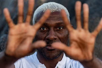 A compelling close-up portrait of an African American man with striking white hair, gazing through his outstretched fingers