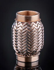 A meticulously woven metallic object gleams against a dark background