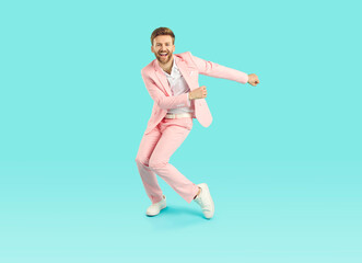 Cheerful young guy dancing and having fun. Full length shot of happy funny handsome man wearing pink suit dancing isolated on blue turquoise color background. Party, fashion concept