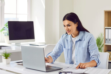 Positive woman works with papers and a laptop at home office or a traditional workspace. Her commitment to productivity seamlessly blends online technology and traditional paperwork.