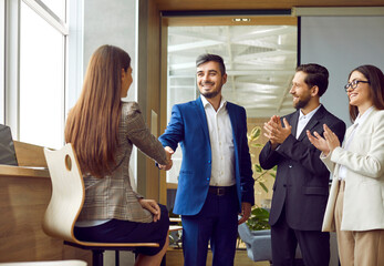 Group of young business people exchange smiles and handshakes in the office. Professionals team symbolizes the triumph of teamwork, success and the strength of modern work partnership.