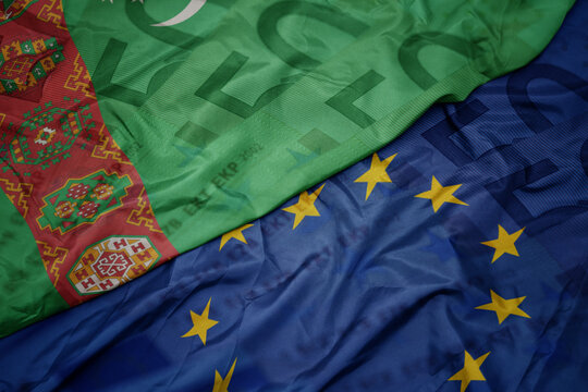 waving colorful flag of european union and flag of turkmenistan on a euro money banknotes background. finance concept.