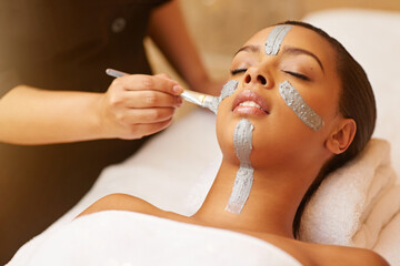 Woman, relax and face mask with brush at salon for beauty, skincare or anti aging on massage bed....