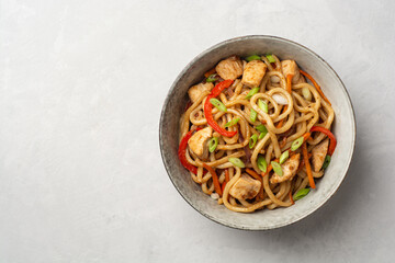 Stir fried udon noodles with chicken and vegetables in bowl on concrete background