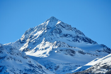 A mountain peak covered in a blanket of snow against a clear blue sky