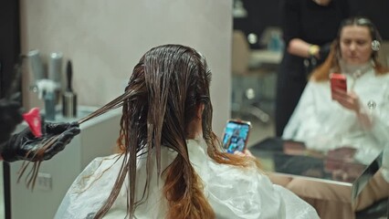 The girl uses the phone while dyeing her hair with percuras. Caring for the appearance of the Dyfstyle beauty salon, solving problems during the beauty procedure on a smartphone. High quality 4k 
