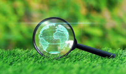 Magnifying glass focused on digital earth globe on the grass in green garden background. Business...