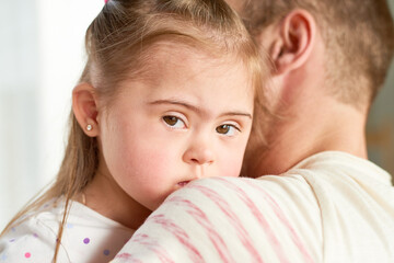 Close up of father holding cute little girl with Down syndrome looking away from camera