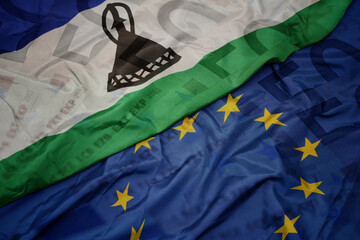 waving colorful flag of european union and flag of lesotho on a euro money banknotes background....