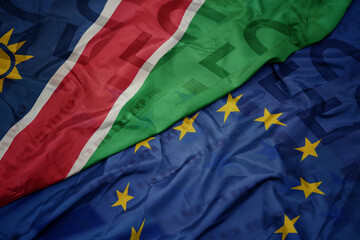 waving colorful flag of european union and flag of namibia on a euro money banknotes background. finance concept.