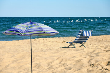 Relaxing beach scene with a blue and white striped beach chair and a striped umbrella. Solitude on a tranquil beach.