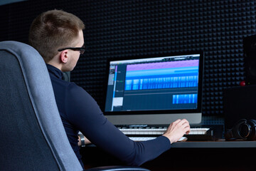 Concentrated music producer editing audio track on computer adding new effect using synthesizer in studio