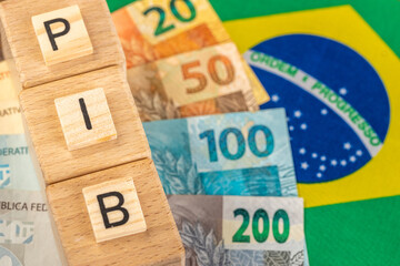 The word PIB (Gross Domestic Product) written on wooden cubes with Brazilian real money in yellow,...
