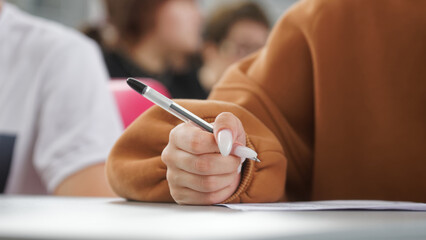 A girl writes a dictation or fills out documents in the classroom, sitting at a desk next to other...