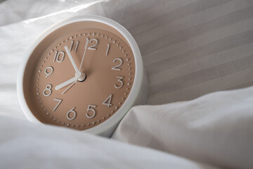 Alarm clock in bed with white blanket, top view, early rise concept, insomnia, daily routine and healthy sleep. Health concept