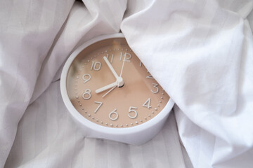 Alarm clock in bed with white blanket, top view, early rise concept, insomnia, daily routine and...