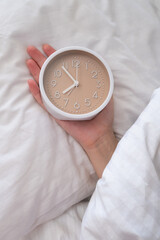 Woman lies on the bed under a blanket and turns off the alarm clock in the morning. Top view, early...