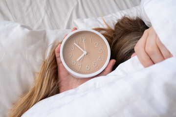 Woman lies on the bed under a blanket and turns off the alarm clock in the morning. Top view, early...