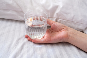 A glass of water next to a girl sleeping in bed. Happy morning. Woman in pyjamas. Healthy lifestyle, wellness. Proper nutrition. Drinking water. Morning with water. Sunlight on linens. Pillow, blanket