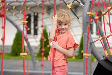 Cheerful child playing and having fun in an outdoor playground. A cute curly-haired smiling girl 6...