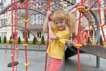 Cheerful child playing and having fun in an outdoor playground. A cute curly-haired smiling girl 6...