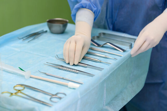 Surgical instruments in the operating room. A nurse in a surgical suit and gloves is preparing for a tooth implant operation. Dental probe, tweezers, scalpel, needle holder, rasps on instrument table.