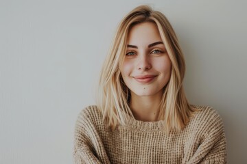 Obraz premium Smiling young woman in a cozy sweater against a plain background