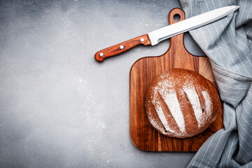 Sourdough rye bread on wooden board, bread knife and black kitchen towel. Gray table background, top view