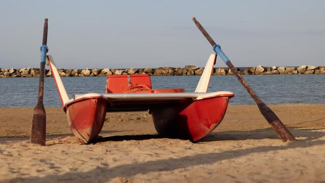 Classic italian rescue boat flanked by oars or rescue rowing catamaran on the sandy beach on the sunset symbolizing preparedness and safety along shoreline.Vacation concept.