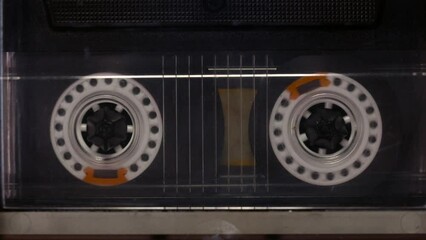 A tape recorder is playing an audio cassette. Close-up. A vintage audio cassette spins on a blank label tape used to record sound in a retro cassette player. Recording of conversations.