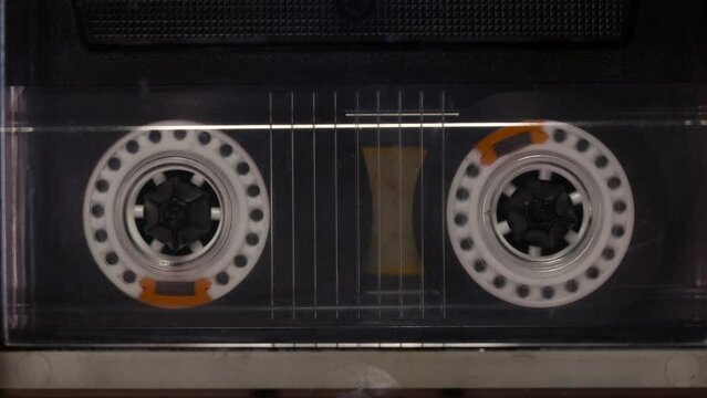 A tape recorder is playing an audio cassette. Close-up. A vintage audio cassette spins on a blank label tape used to record sound in a retro cassette player. Recording of conversations.