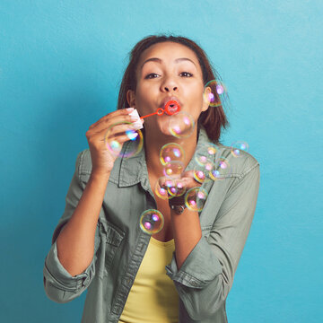 Happy woman, portrait and blowing with bubble wand for soap, fun or playing with magic on a blue studio background. Young female person or model with floating liquid particles in party or celebration