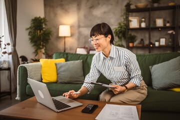 Mature japanese woman hold clipboard and use at laptop work from home