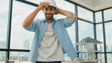Portrait of smart architect engineer wear safety helmet while sitting on table with house model,...