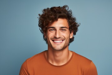 Fototapeta premium A man with curly hair is smiling and wearing an orange shirt