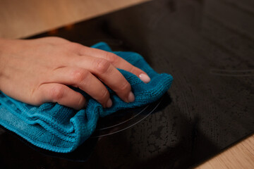 A person is cleaning a black stove top with a blue cloth