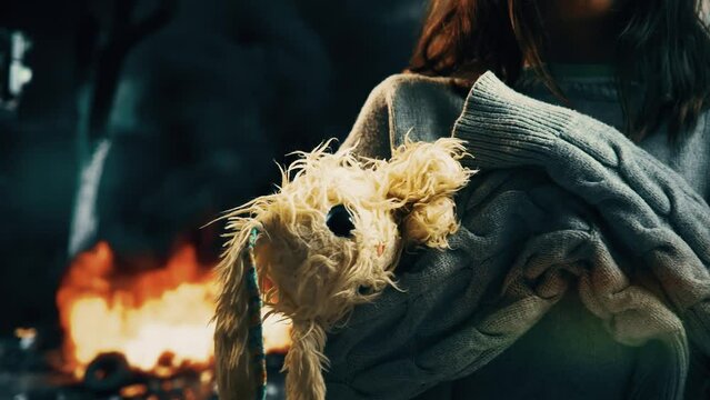 A little girl with her favorite plush toy in her hands against the background of a burning destroyed house. War and children, war crimes, terrorism, no war.