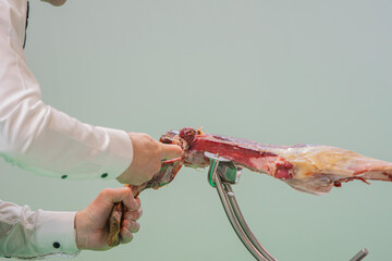 A man is cutting ham with a knife. The meat is bloody and has a lot of blood on it