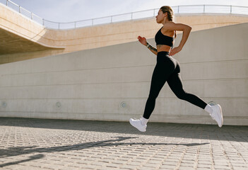 Active woman athlete is jogging on morning on modern building background. Healthy life concept