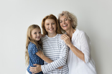 Beautiful multi-generational relative women hugging posing on gray studio background, smile look at camera enjoy their harmonic relationship, friendship and family ties, showing togetherness and unity