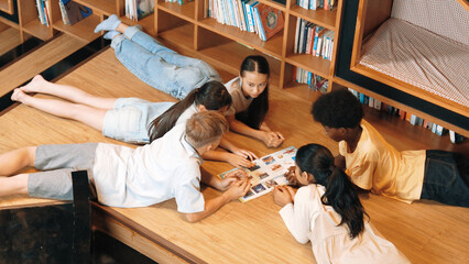 Group of diverse children lying down in circle while reading a book at library. Top view of girl...