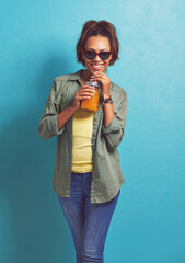 Happy woman, portrait and sunglasses with orange juice for vitamin C or summer fashion on a blue studio background. Female person, brunette or model with smile for citrus drink or fresh beverage