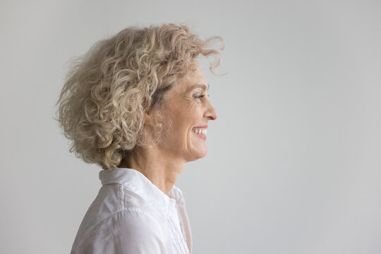 Side profile view head and shoulders of happy middle-aged woman staring straight posing alone against gray studio background with copy space. Services for elderly, optimism, midlife and wise quotes