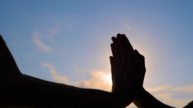 Slow motion: silhouettes of woman and man are giving a high fives hand gesture against the sunset or sunrise sky - close up, sun lens flares. Friendship, celebration, greeting and positive concept