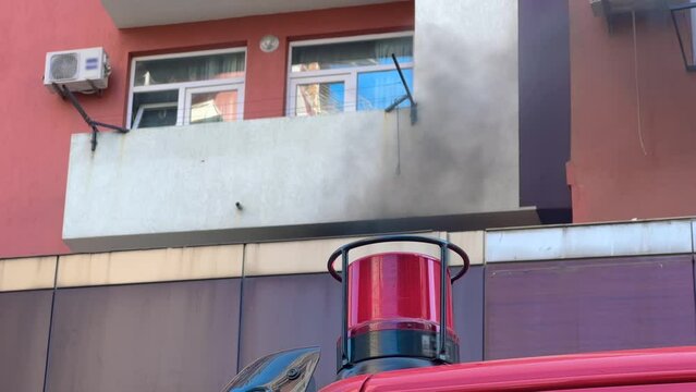 Red flashing signal light on the fire truck, fire engine. Dark smoke from the fire is pouring out of the window of building. Emergency vehicle lighting, firefighting and alarm concept